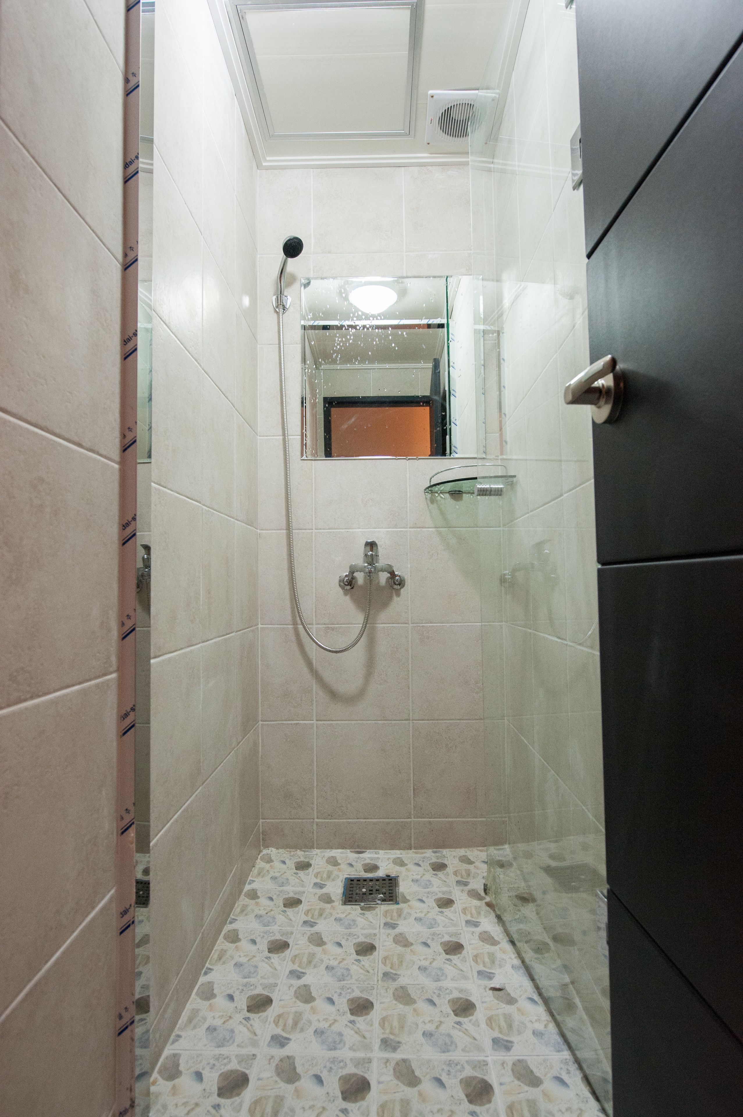 Un baño pequeño con azulejos, una ducha, un estante de vidrio y una puerta.