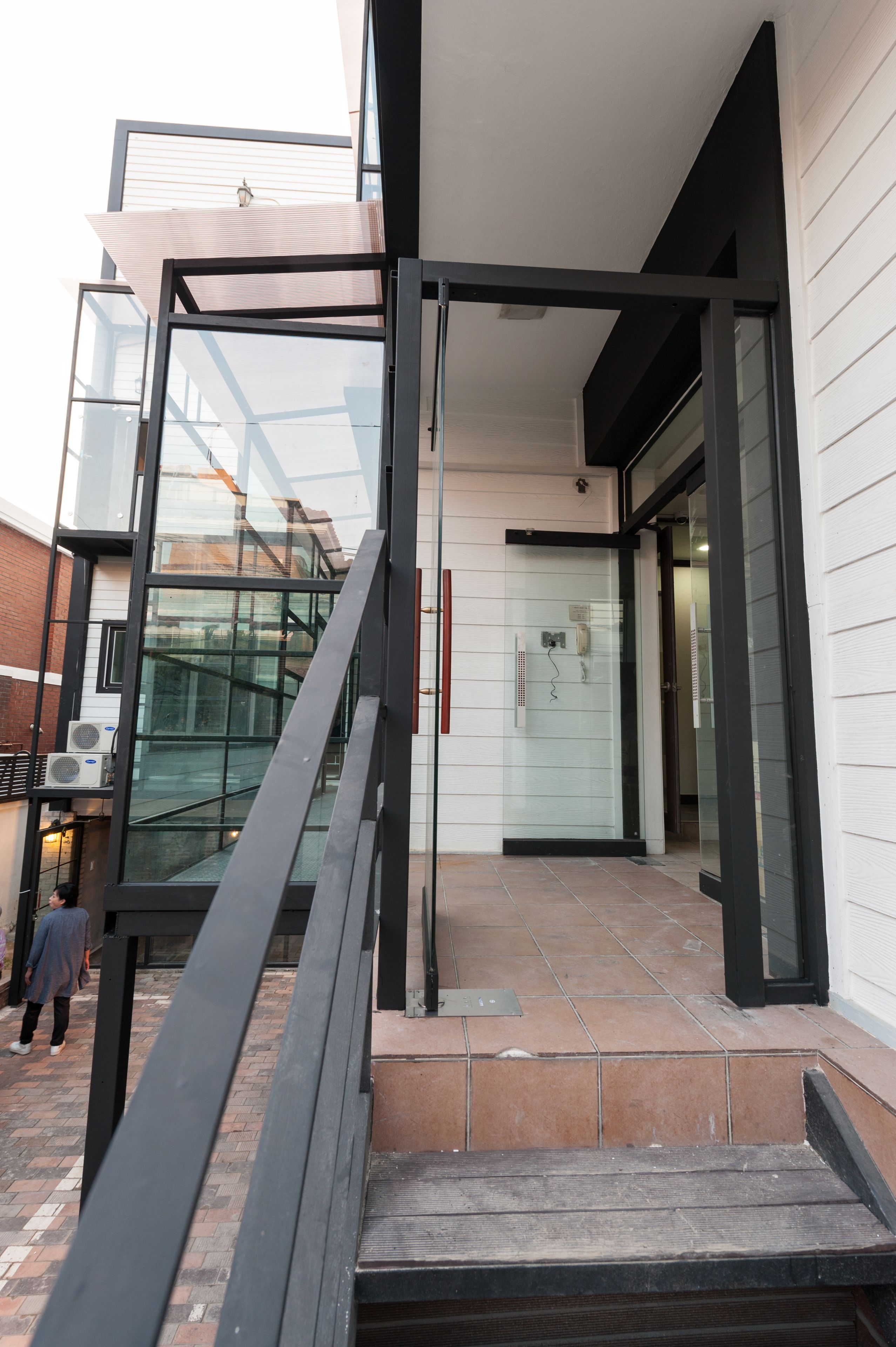 A modern building entrance with glass doors, a metal staircase, and a tiled floor.