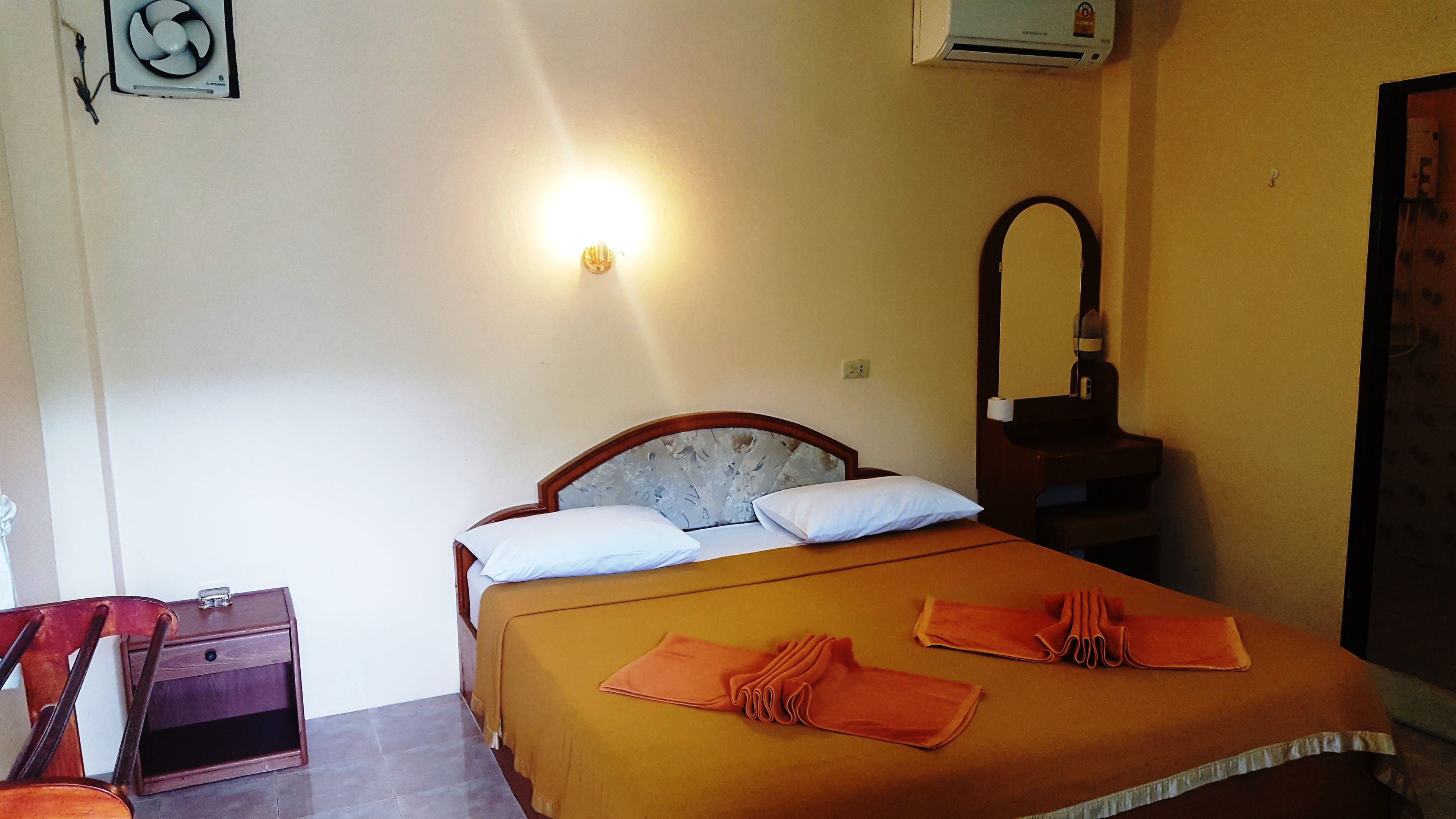 Una cama bien tendida con cabecera, una mesita de noche con lámpara y un aire acondicionado instalado en la pared.