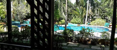 Zona de piscina con vista despejada al agua, rodeada de abundante vegetación y palmeras.