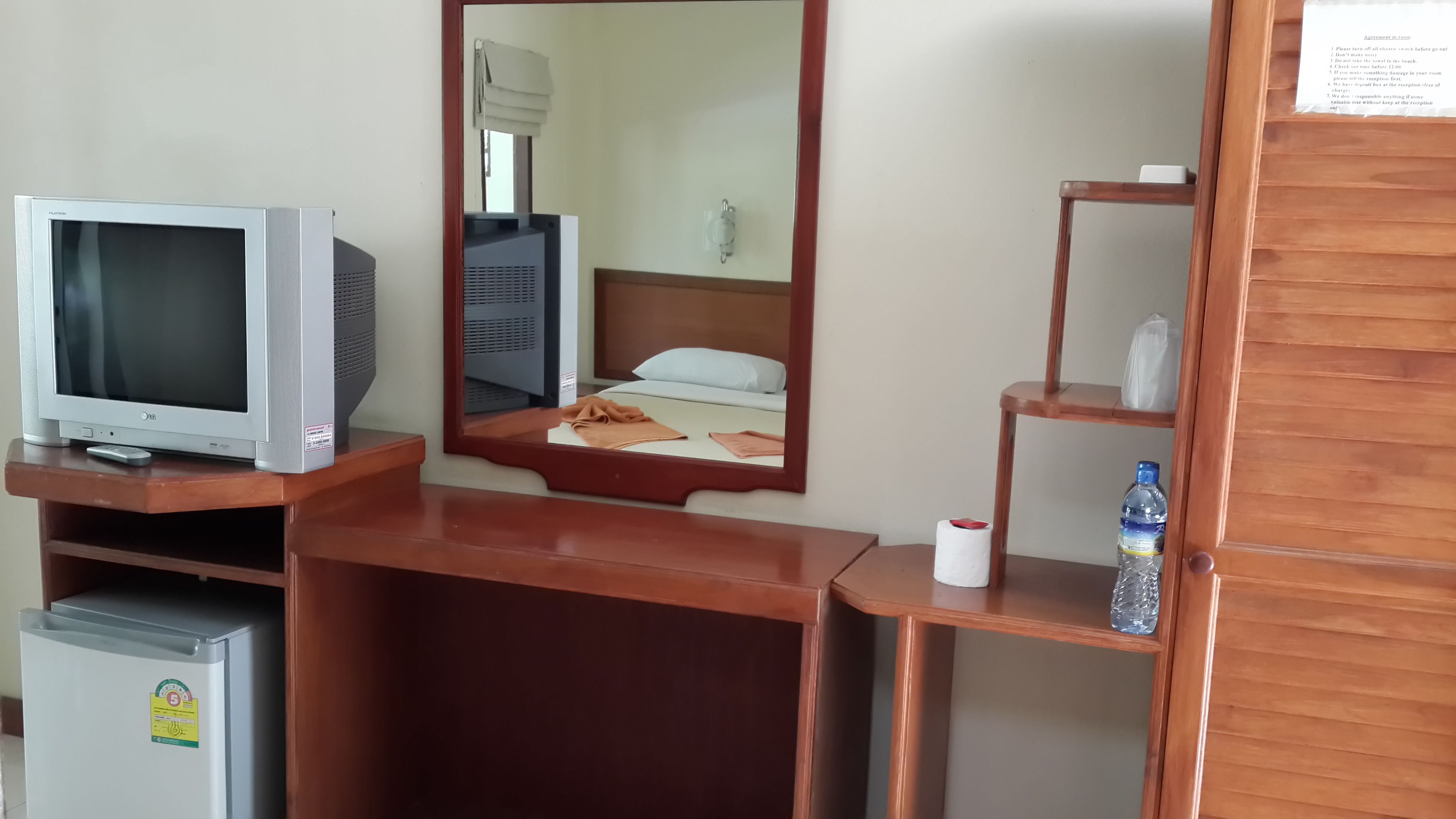 Une chambre d’hôtel équipée d’une télévision, d’un miroir, d’un petit réfrigérateur, d’une bouteille d’eau et d’un rouleau de papier toilette.