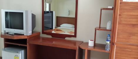 Une chambre d’hôtel équipée d’une télévision, d’un miroir, d’un petit réfrigérateur, d’une bouteille d’eau et d’un rouleau de papier toilette.