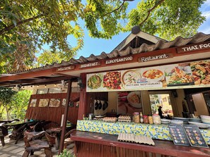 An outdoor Thai food restaurant with a wooden structure, a menu board, and a variety of food items displayed. - Rattana Guesthouse & Bungalow (Koh Samui)