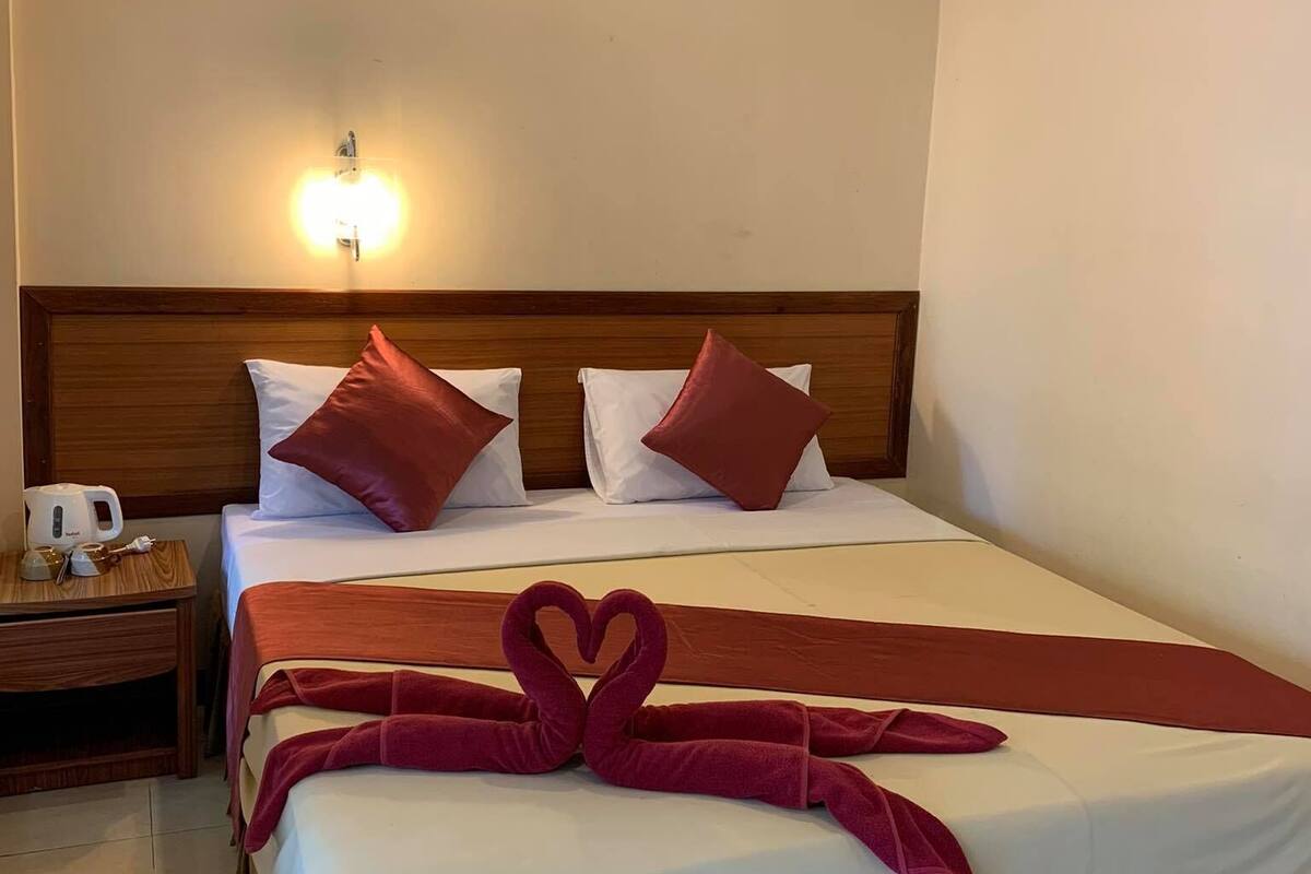 A hotel room with a bed, a nightstand, a lamp, and a towel art on the bed.