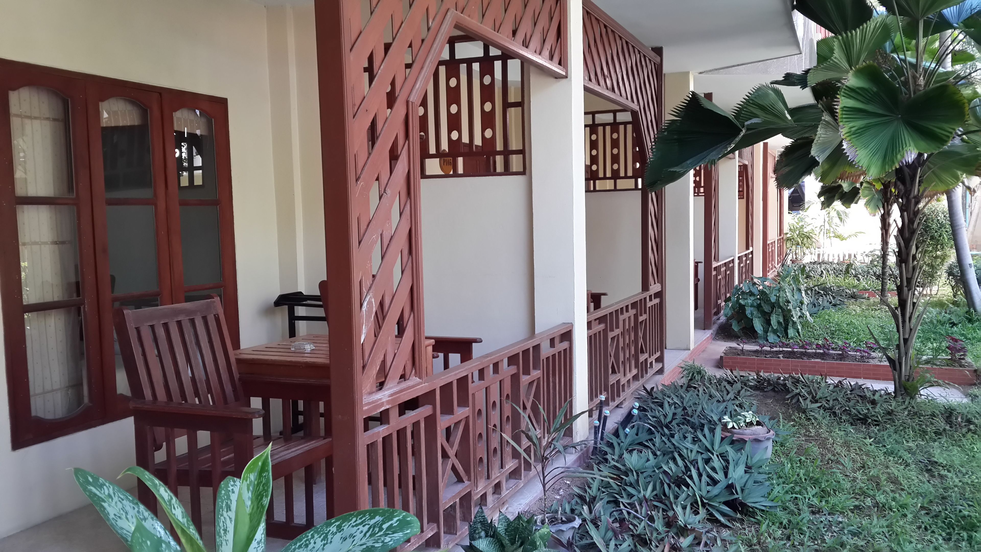 Un espacio de estar al aire libre cubierto, con mobiliario de madera y una valla decorativa de madera.