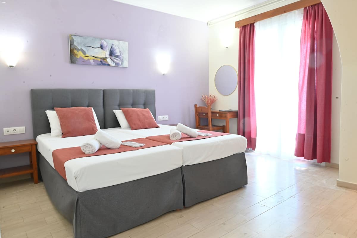 Una cama doble con cabecera gris y ropa de cama blanca, una mesita de noche, una pequeña mesa de madera con espejo y un cuadro en la pared.
