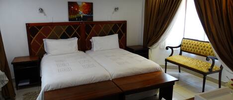 A hotel room with a double bed, a wooden headboard, a bench, a small table, and a painting on the wall.
