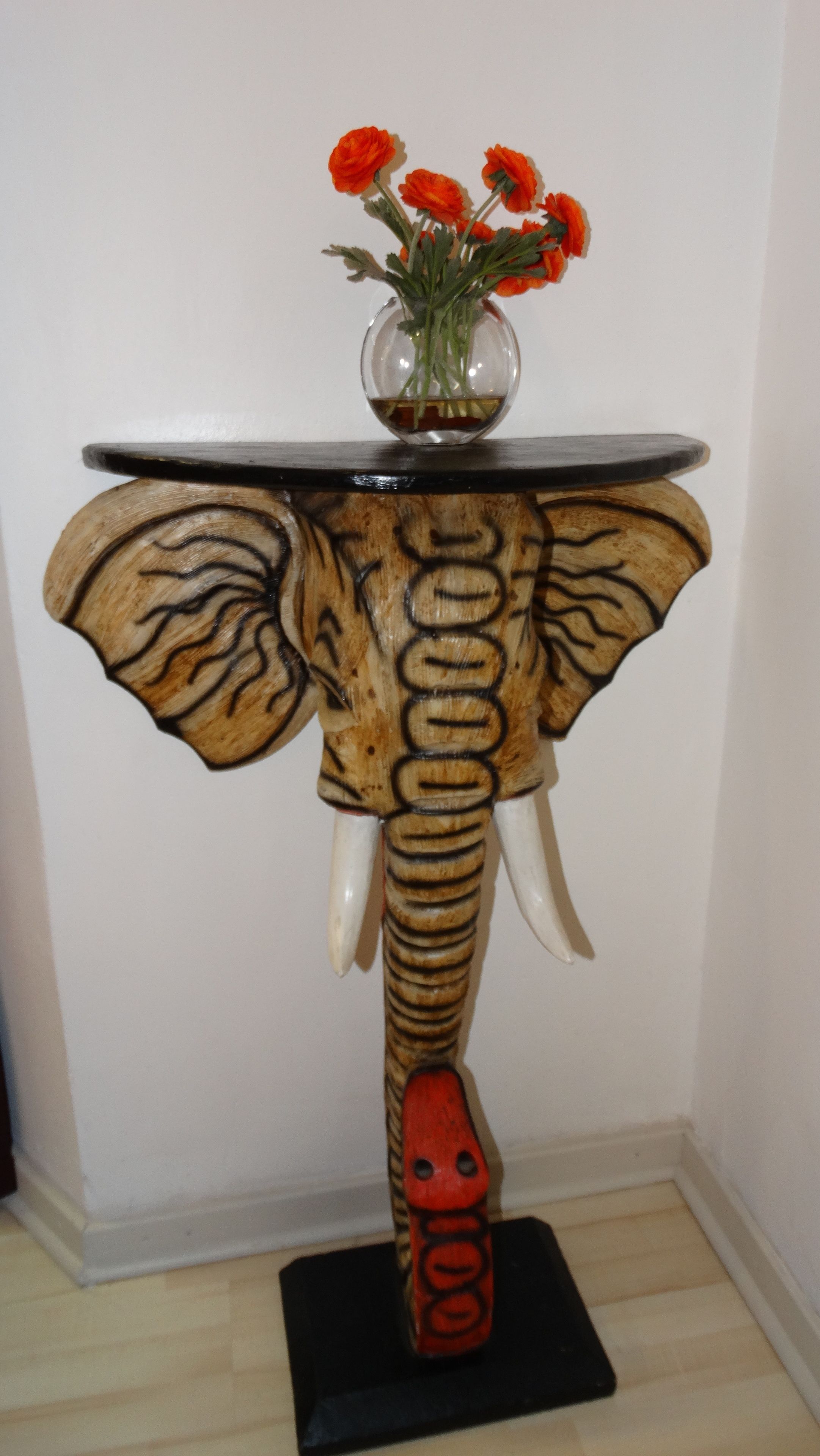 A wooden elephant-shaped table with a vase of flowers on top.