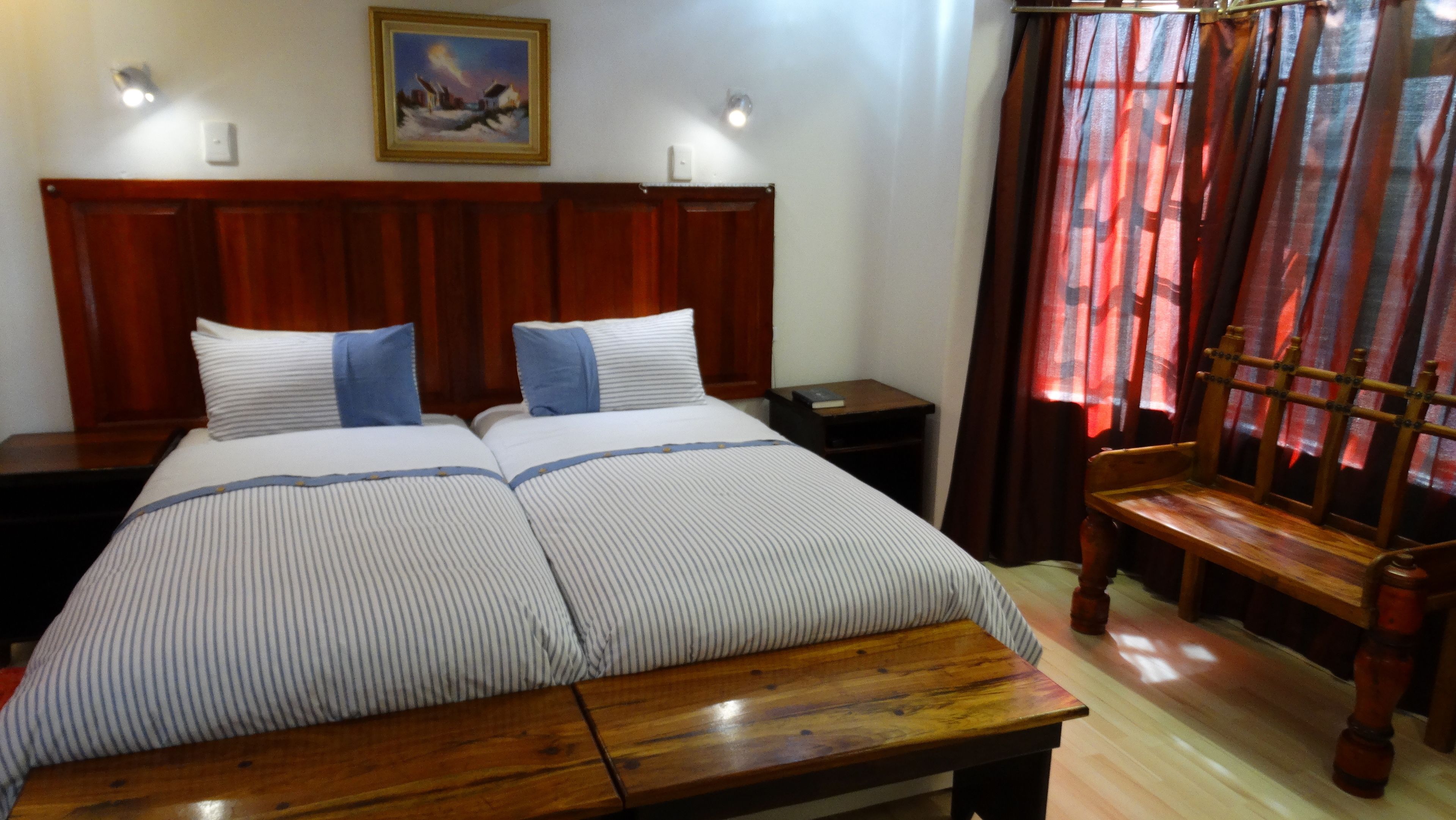 Ein Doppelbett mit gestreifter Bettwäsche, ein Holz-Kopfteil, Nachttische, ein kleiner Beistelltisch und ein Fenster mit roten Vorhängen.