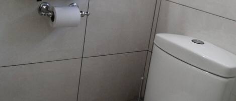 A bathroom with a toilet, a towel rack with folded towels, and a toilet paper holder.