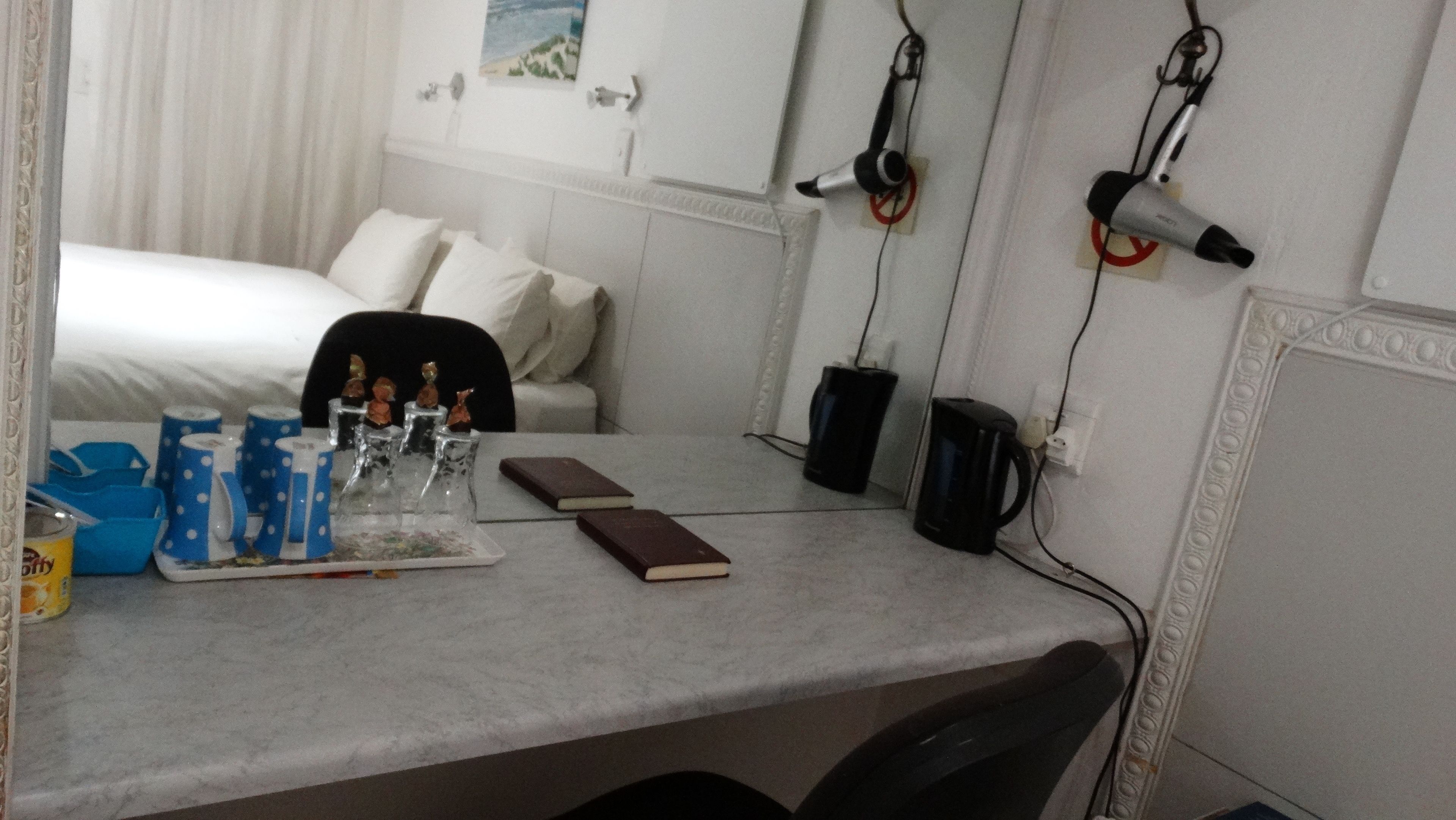 A hotel room with a bed, a desk with a notebook, a coffee maker, and a hairdryer on the wall.