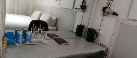A hotel room with a bed, a desk with a notebook, a coffee maker, and a hairdryer on the wall.