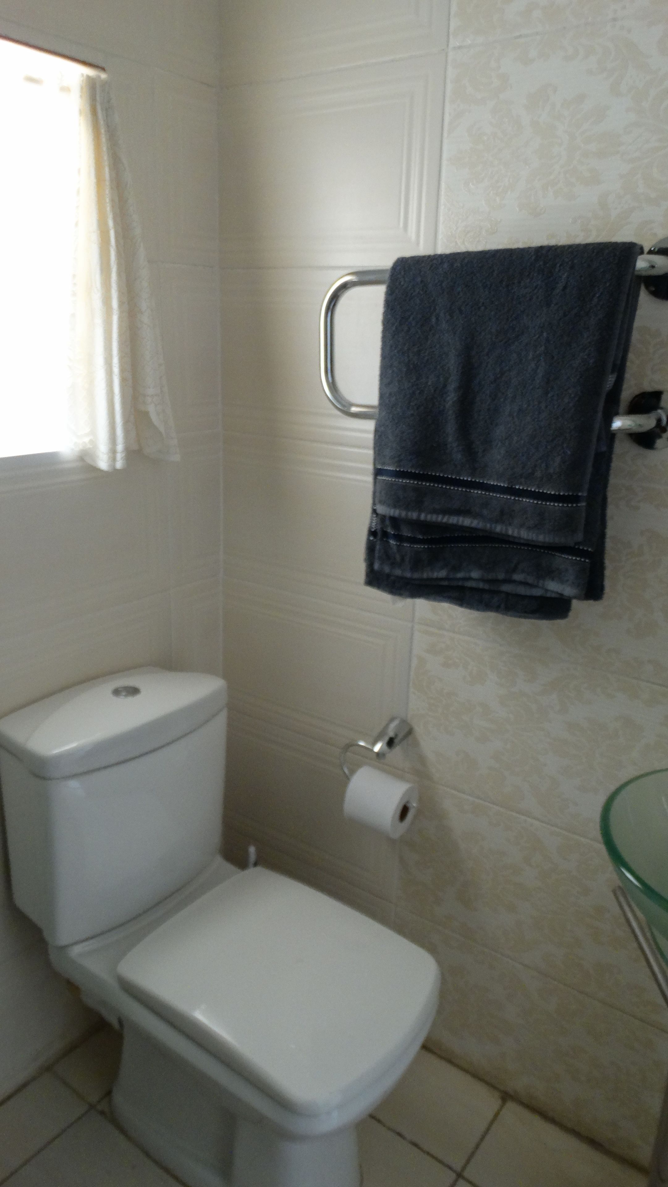 A bathroom with a toilet, a towel rack with a towel, and a toilet paper holder.
