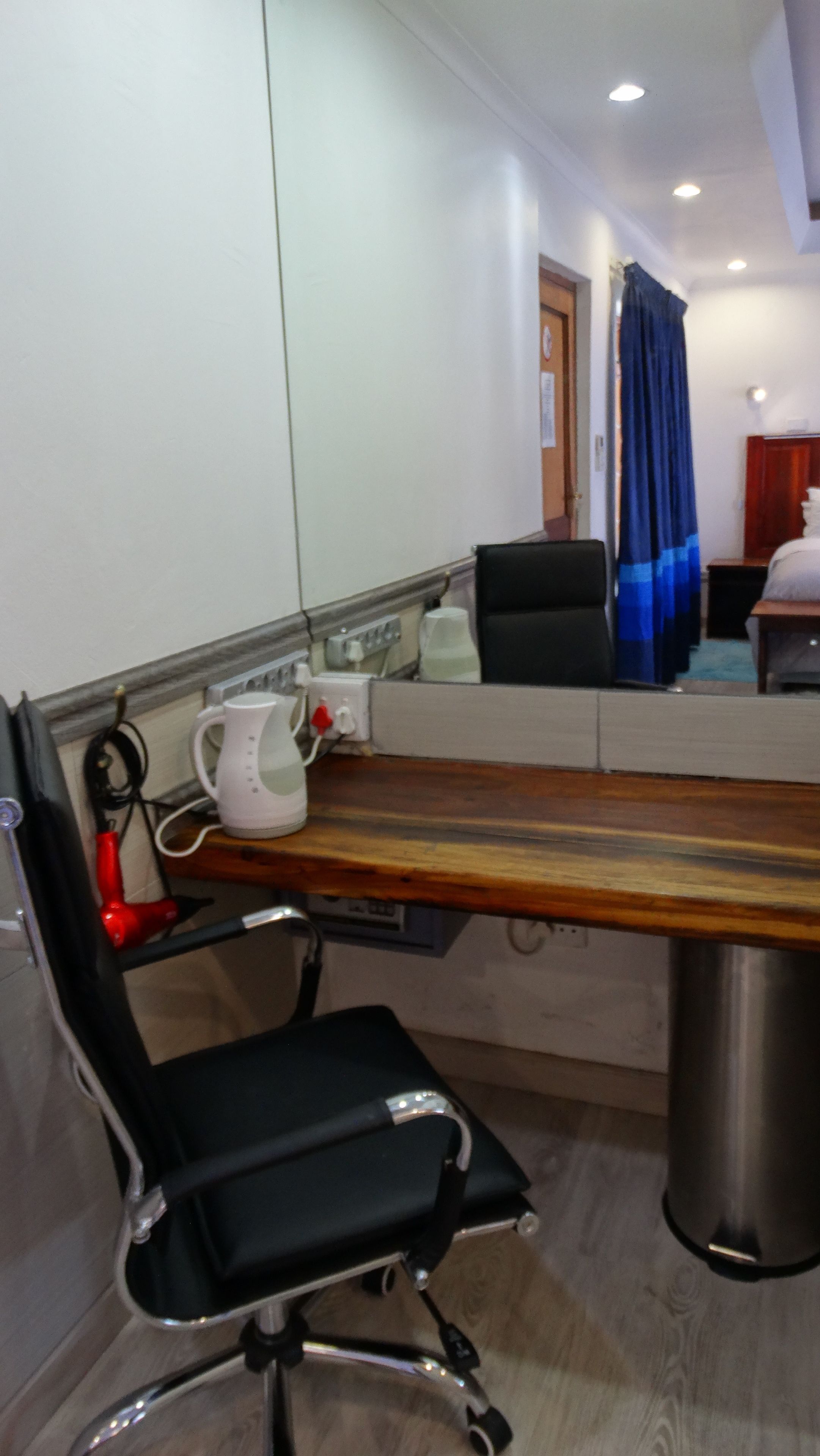 A conference room with a wooden table, a black office chair, a white kettle, and a blue curtain.