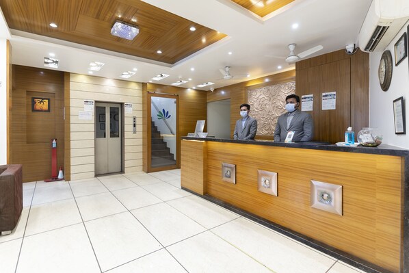 A hotel reception area with a wooden reception desk, a staircase, and a clock on the wall.