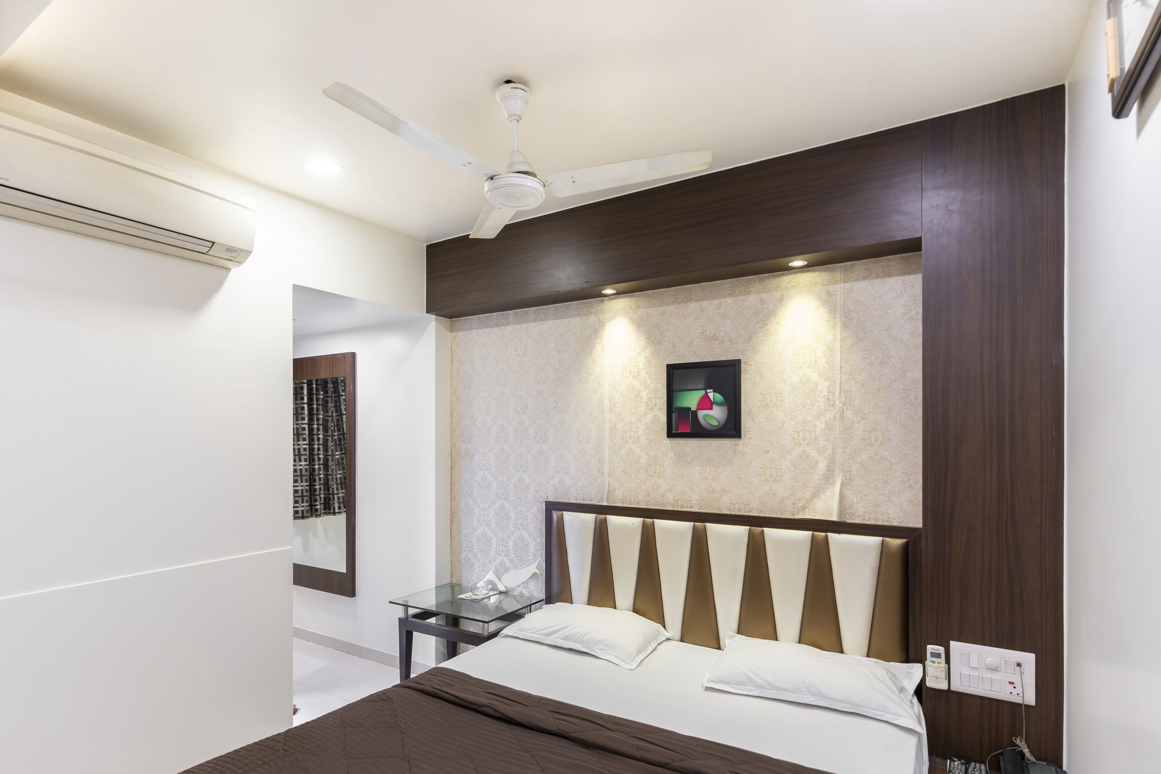 A modern hotel room with a bed, a nightstand, a ceiling fan, and a wall-mounted artwork.