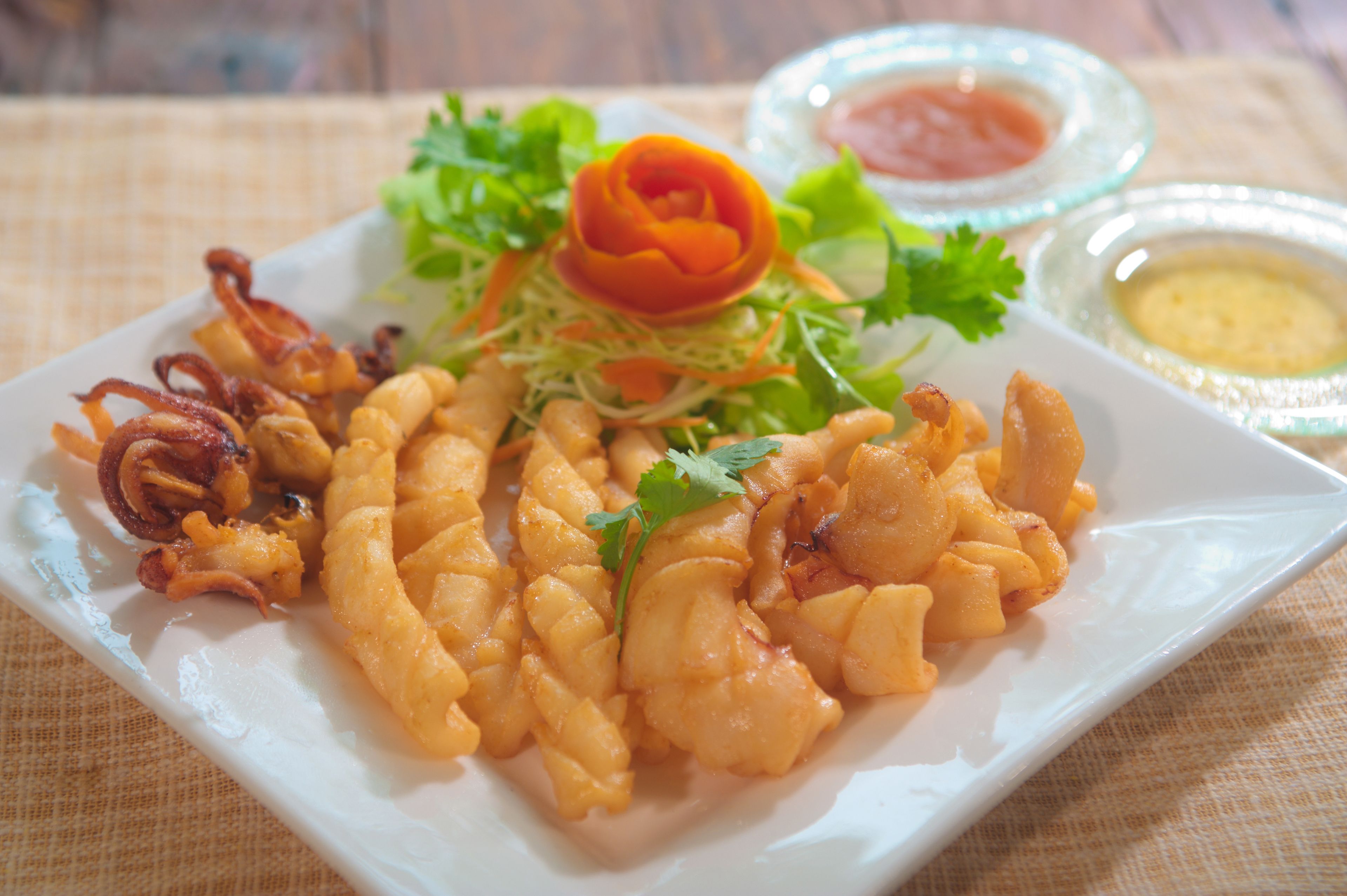 A plate of food with fried items and a salad, accompanied by two small bowls of dipping sauces.