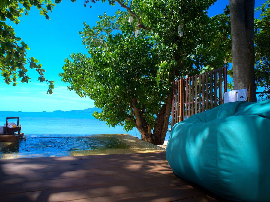 Una terraza de madera con un sillón de peluche color turquesa, un bote pequeño y un árbol que da sombra.