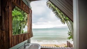 Ein Badezimmer mit Waschtisch aus Holz und einem großen Spiegel, mit Blick auf einen Strand mit Wellen und blauem Himmel.