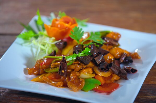 A square plate with a colorful stir-fry dish, garnished with herbs and vegetables. - @ Samui Haus (Koh Samui)