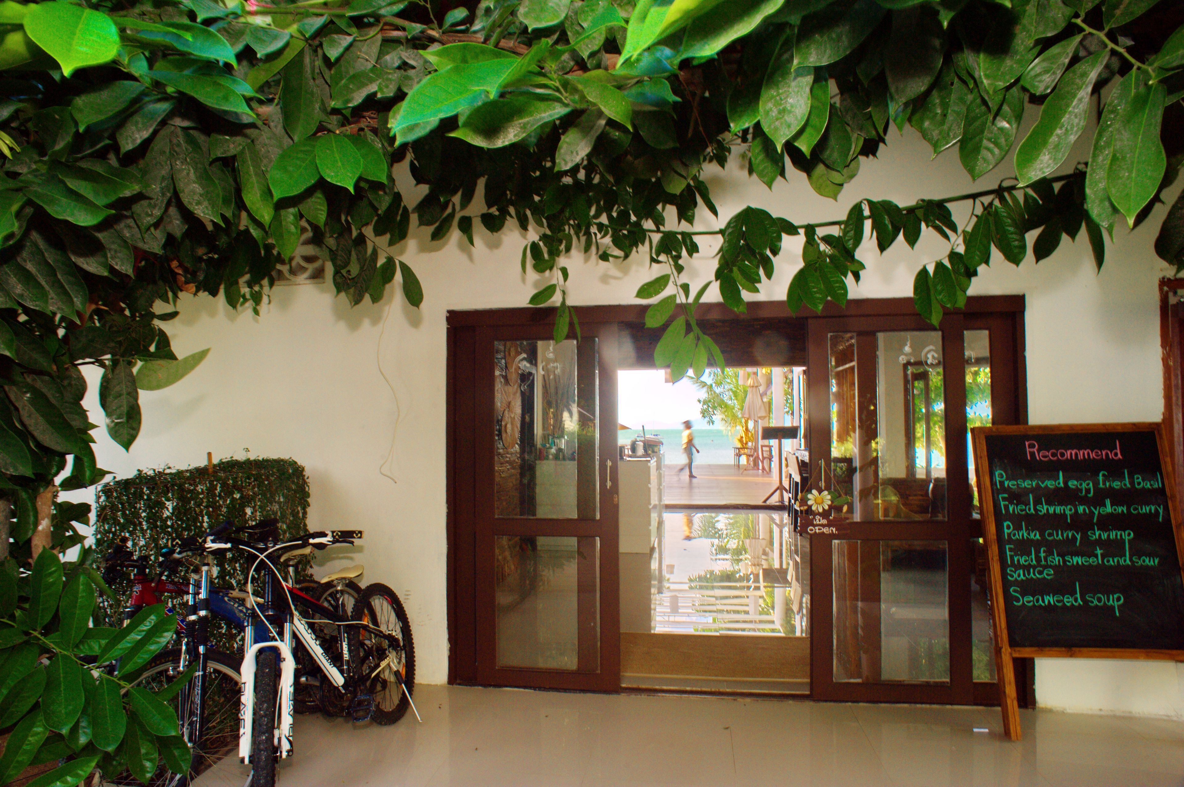 A restaurant entrance with a glass door, bicycles parked outside, and a menu board listing dishes.