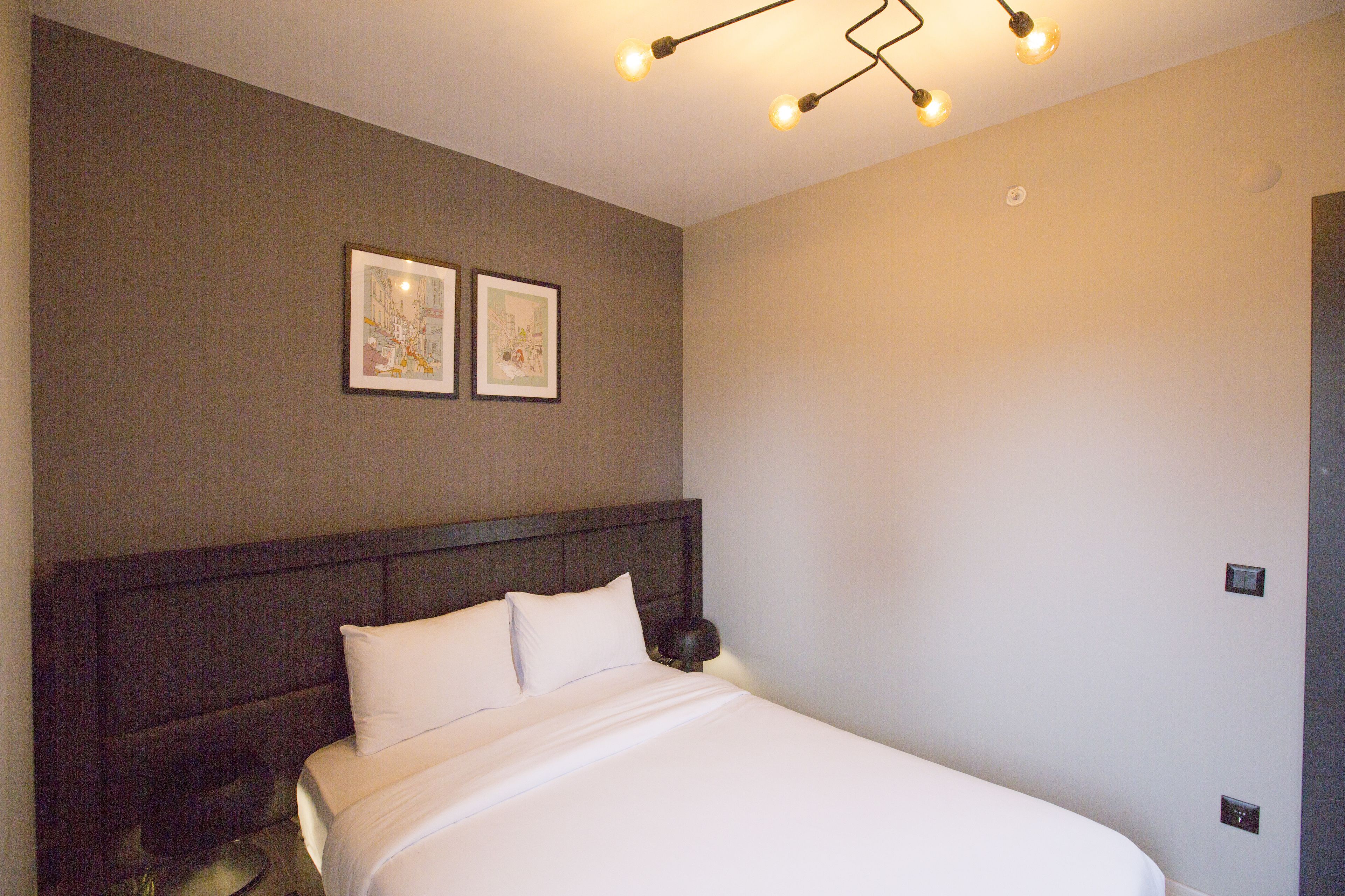 A neatly made bed with a headboard, two framed pictures on the wall, and a modern light fixture above.