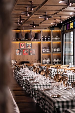 A restaurant with checkered tablecloths, wooden walls, and hanging pendant lights.