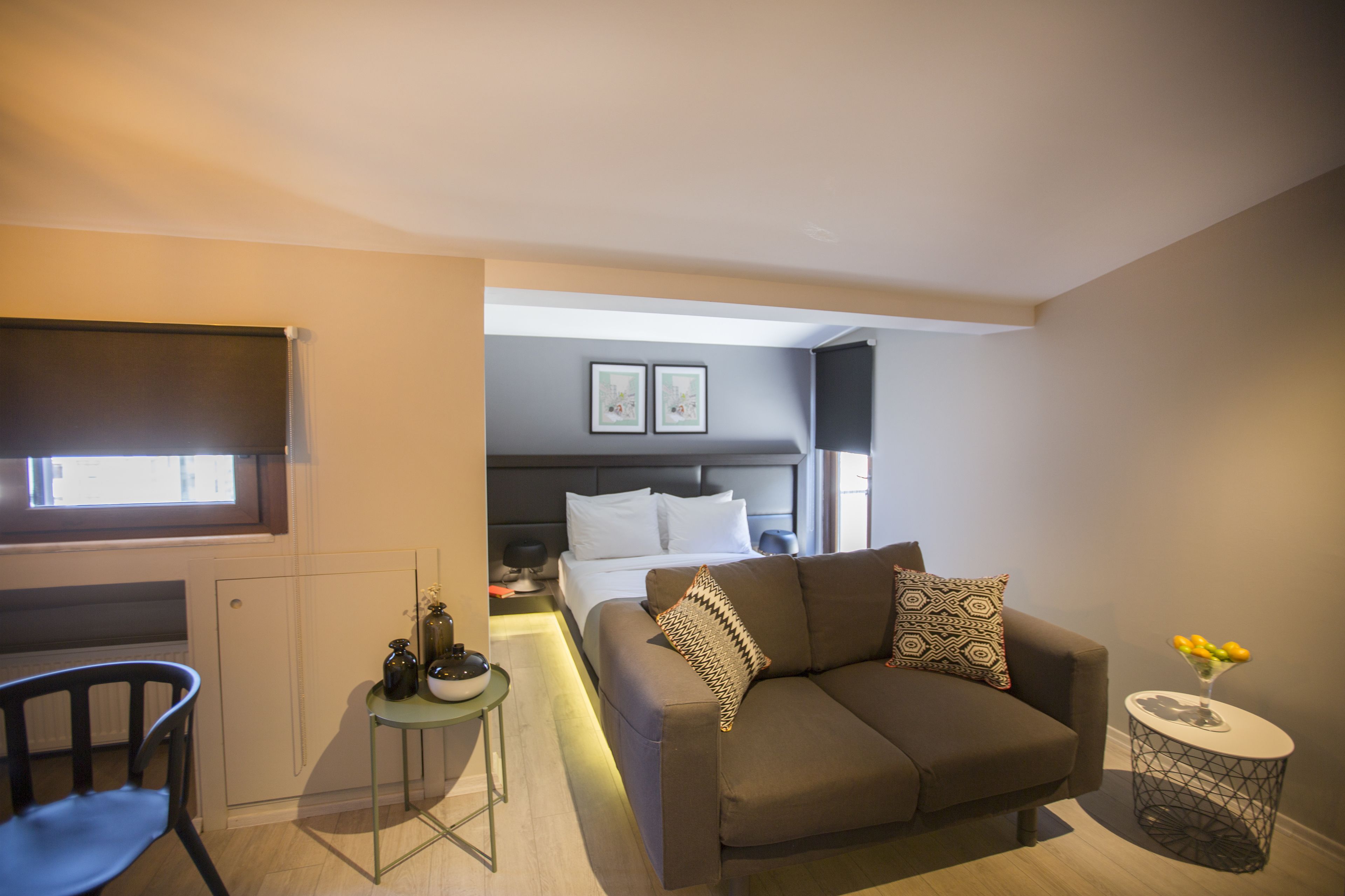 A compact hotel room with a sofa, a small table, a chair, a bed, and a window.