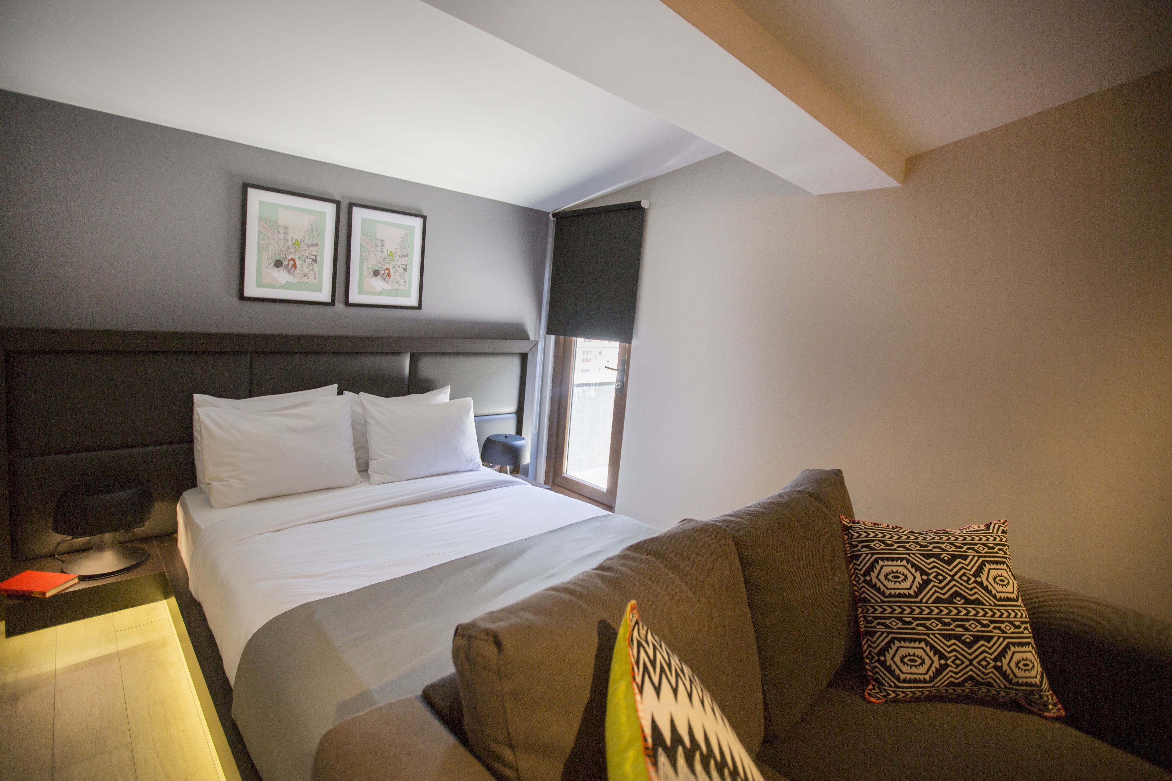 A hotel room with a bed, a sofa, a nightstand, and two framed pictures on the wall.