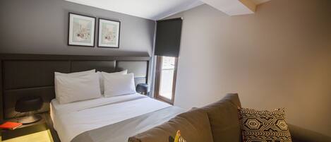 A hotel room with a bed, a sofa, a nightstand, and two framed pictures on the wall.