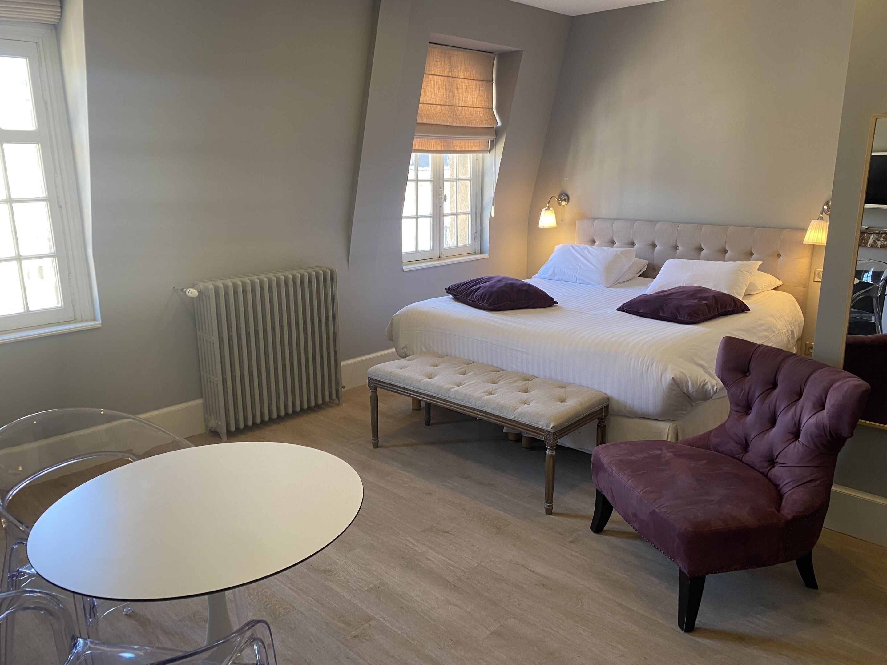 Un dormitorio con cama, mesitas de noche, un banco, una silla y una ventana.