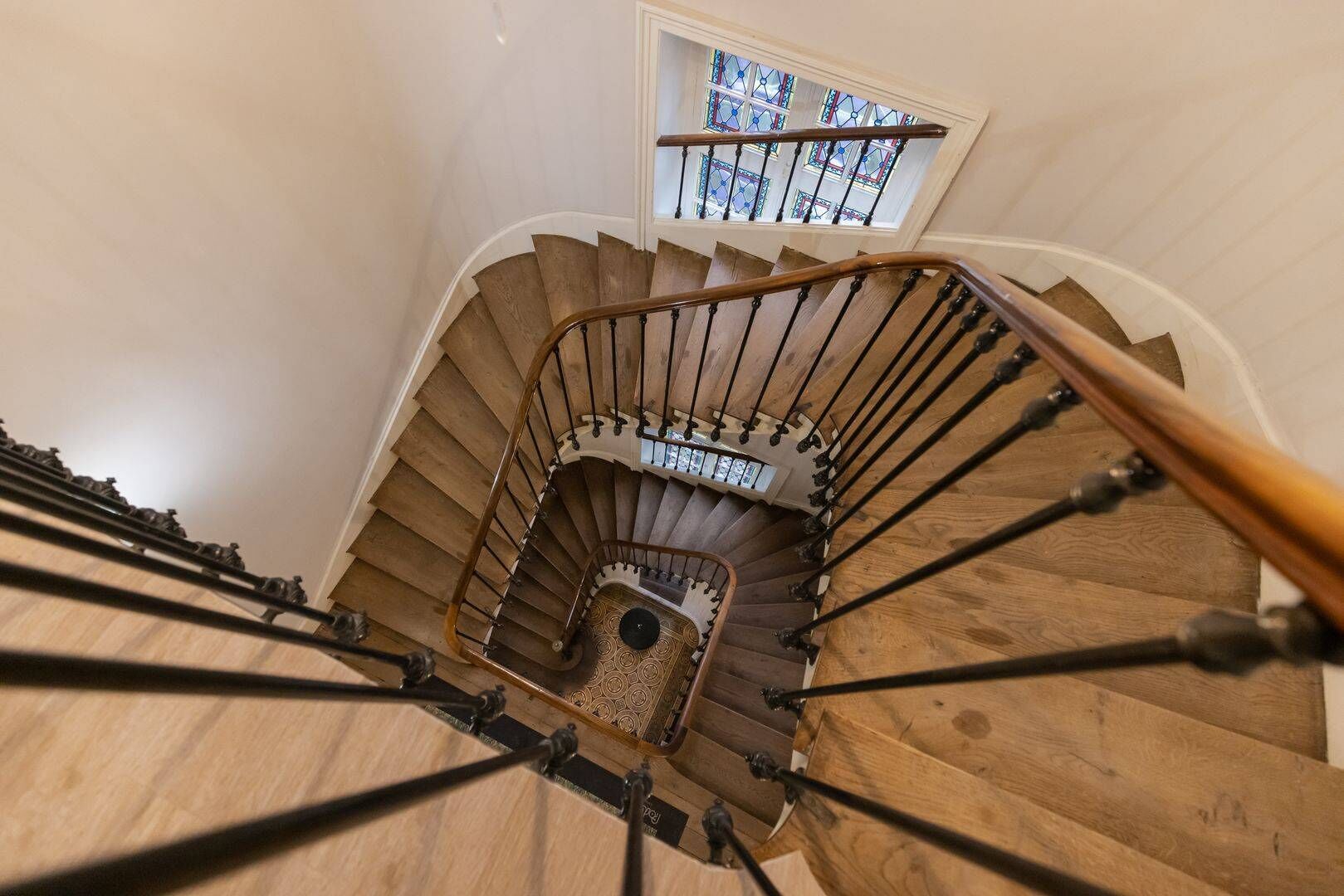 Eine Wendeltreppe mit Holzbodenstufen und Metallgeländern, die zu einer Zwischenebene mit einem kleinen, bleiverglasten Fenster führt.