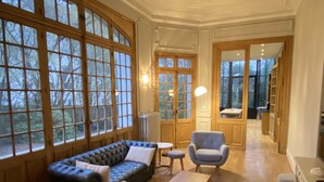 Une pièce spacieuse avec de grandes fenêtres, un canapé bleu, un fauteuil gris et une petite table.