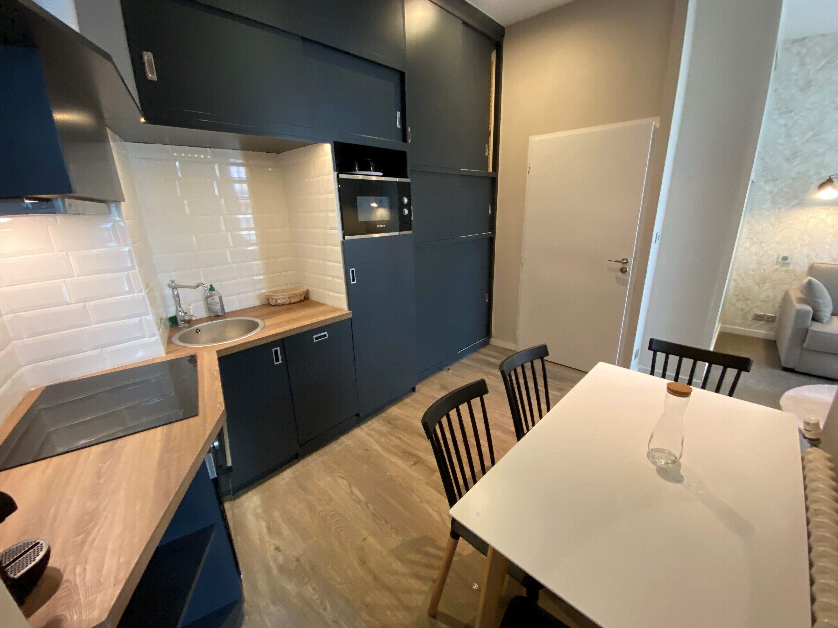 Una cocina moderna con armarios oscuros, una encimera blanca y una mesa de comedor de madera con sillas.