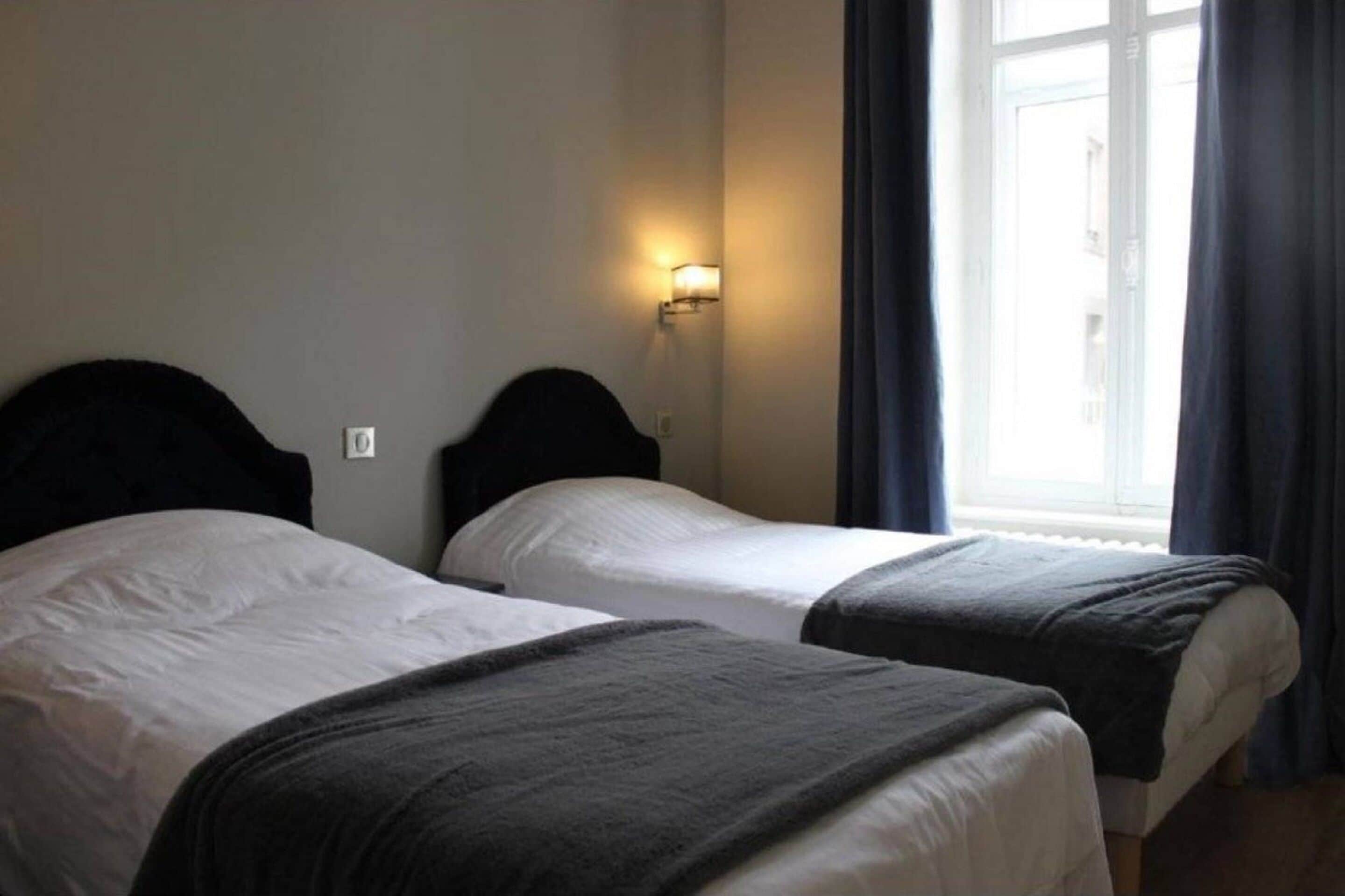Ein Hotelzimmer mit zwei Einzelbetten, einem Nachttisch, einer Wandlampe und einem Fenster mit Vorhängen.