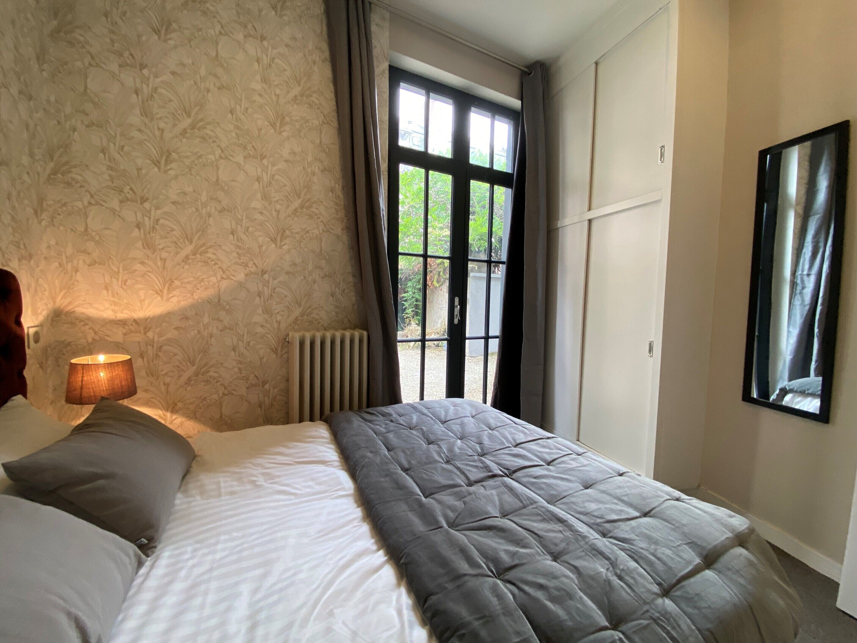 Une chambre à coucher avec un lit, un radiateur, une fenêtre avec des rideaux et un miroir fixé au mur.