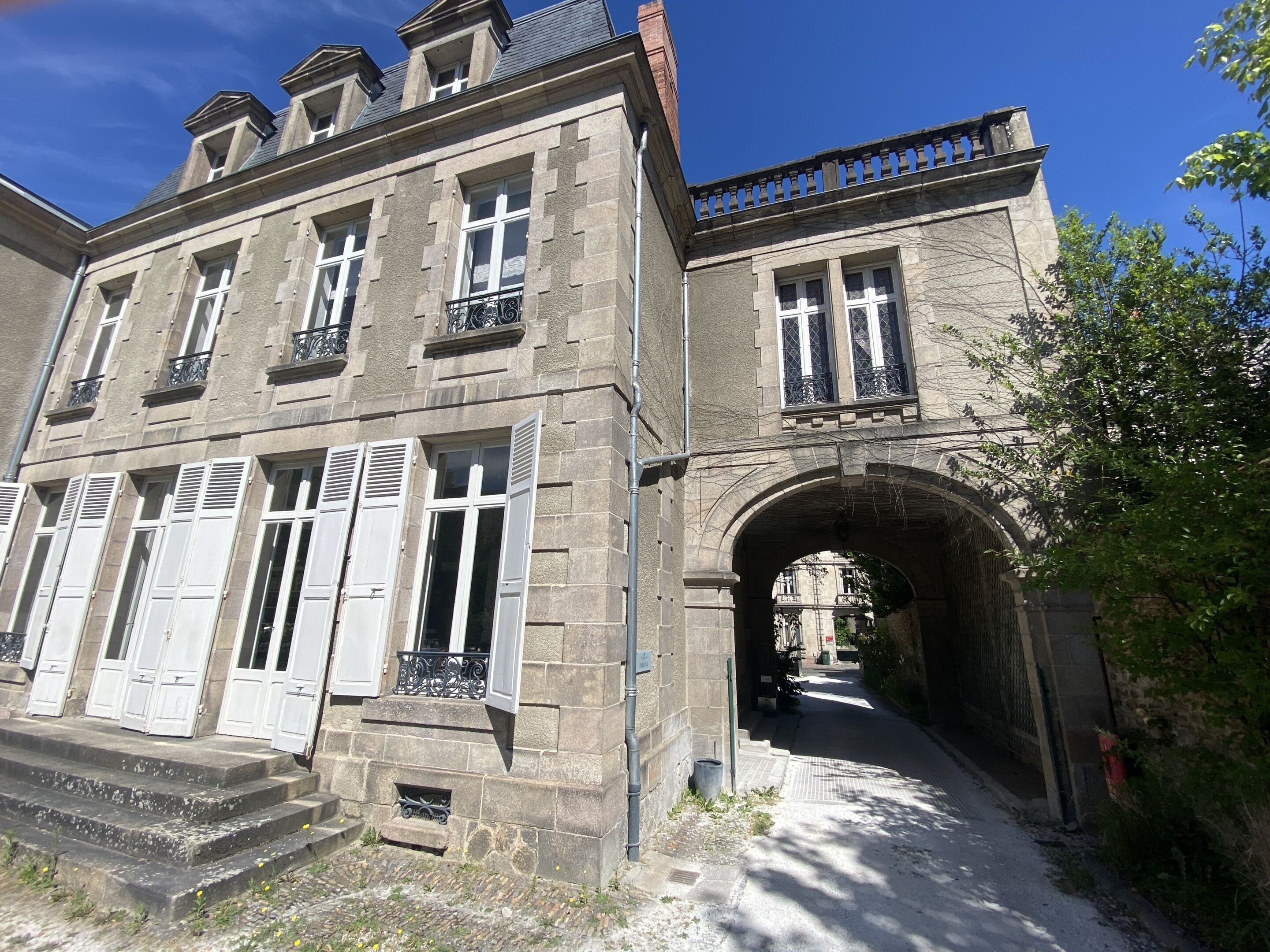 Un bâtiment historique en pierre, doté de nombreuses fenêtres, d’une arche centrale et d’un chemin piétonnier pavé.