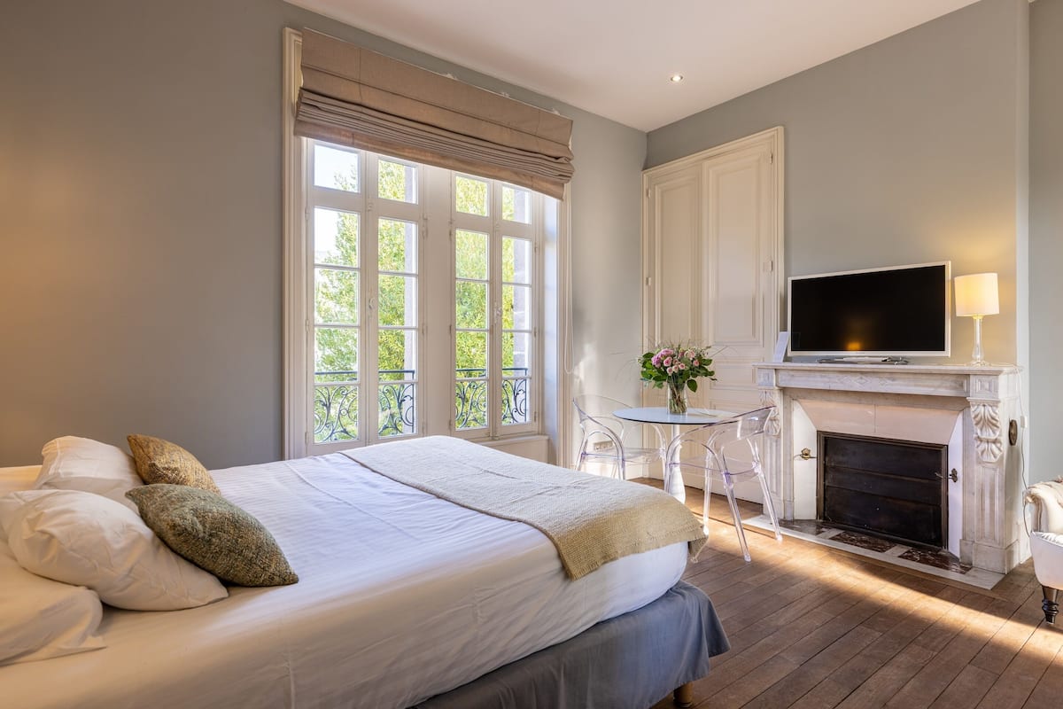 A bedroom with a bed, a TV, a fireplace, and a window with curtains.