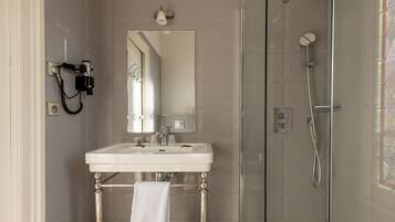 A bathroom with a glass shower enclosure, a white sink with a mirror above it, and a hairdryer mounted on the wall.