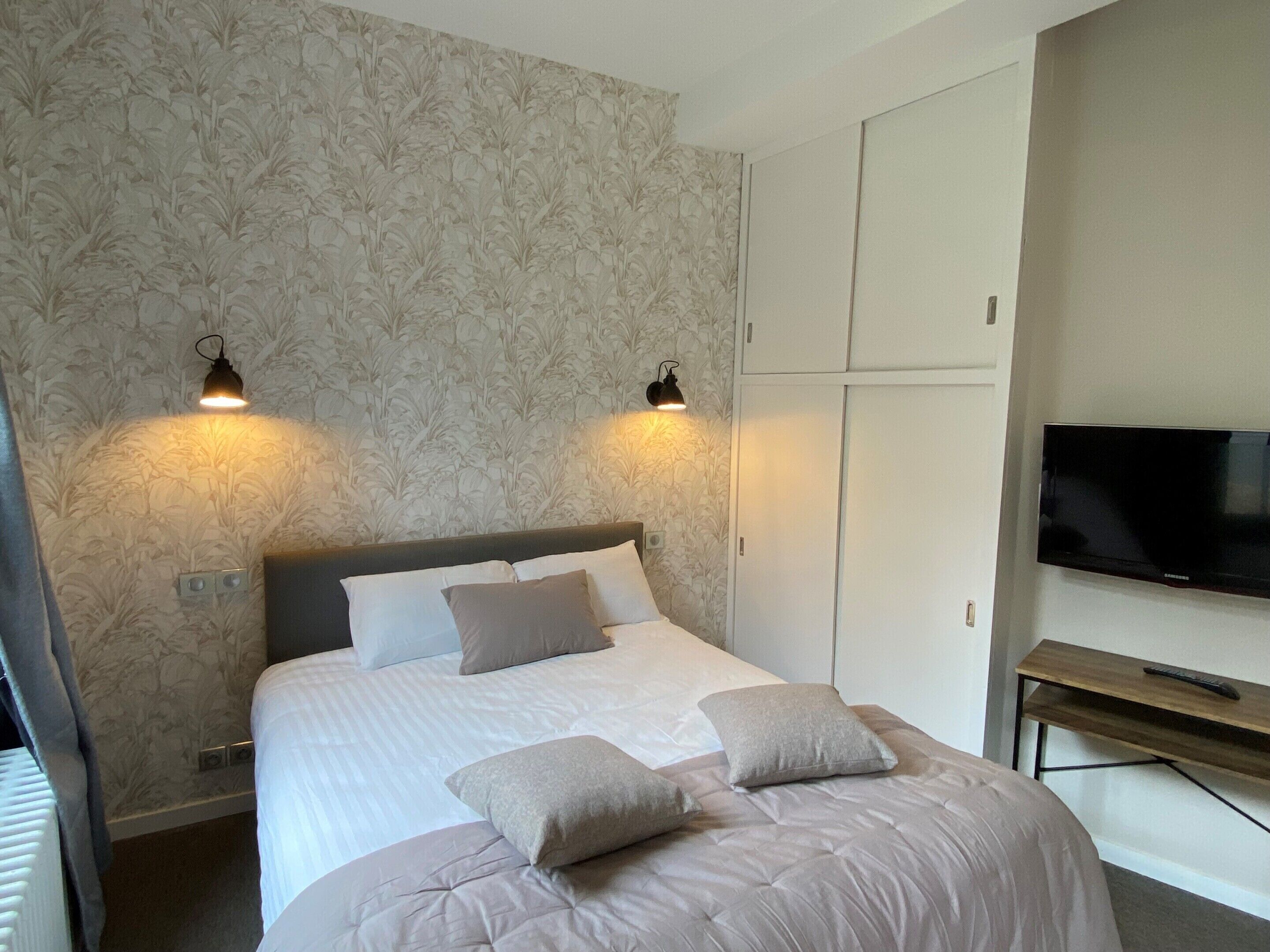 A neatly made bed with pillows, a wall-mounted TV, and two wall sconces.
