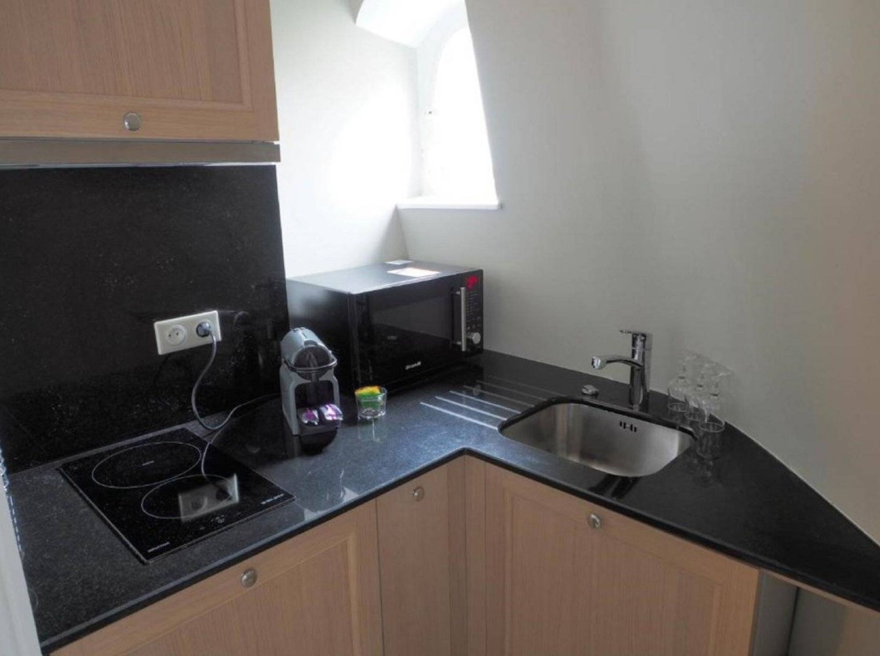 A compact kitchen with a black countertop, a stainless steel sink, a microwave, and a coffee maker.