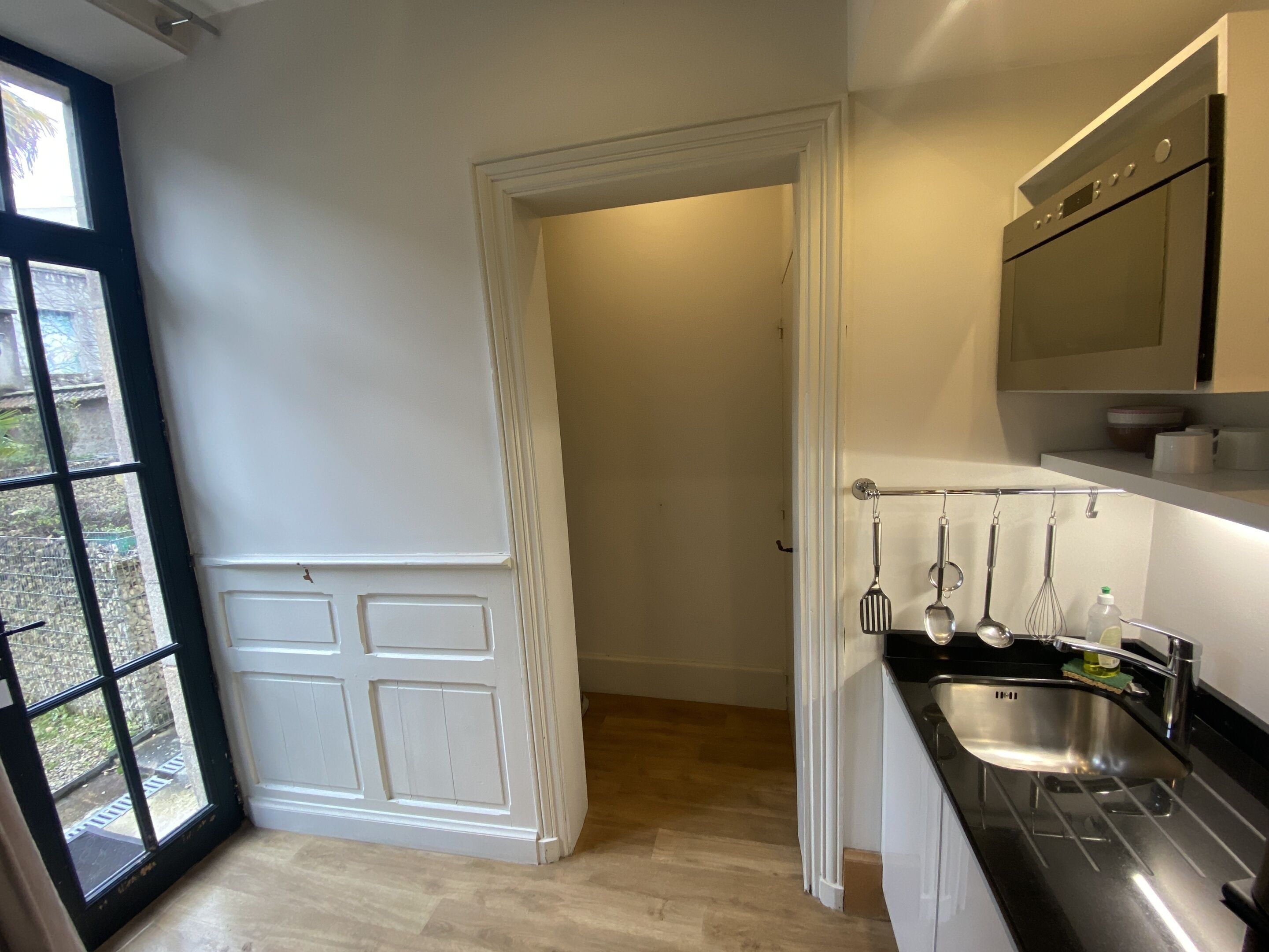 Een moderne keuken met een roestvrijstalen spoelbak, hangende keukengerei en een ingebouwde oven.