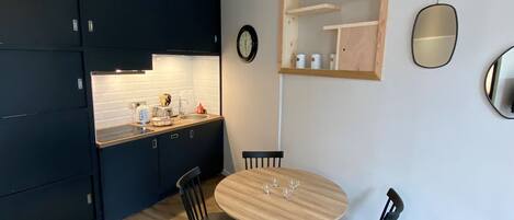 A compact kitchen with dark cabinets, a wooden countertop, a round dining table with four chairs, and a wall-mounted shelf with a mirror.