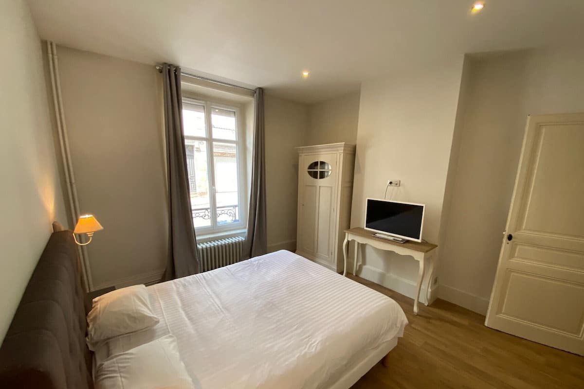 A bedroom with a bed, a TV on a small table, a wardrobe, and a window with curtains.