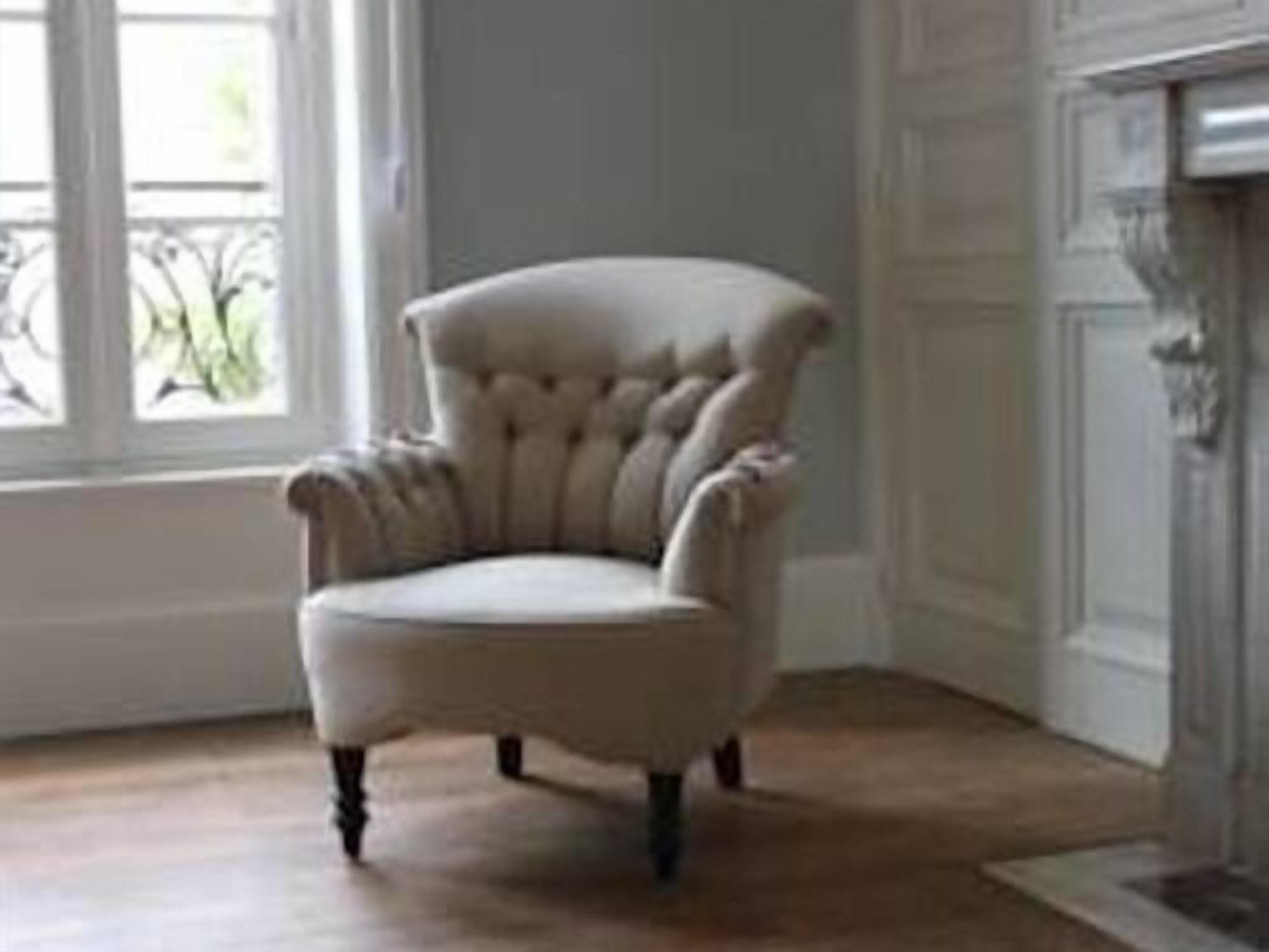 Een stoel in een kamer met een houten vloer en een raam met uitzicht op groen.