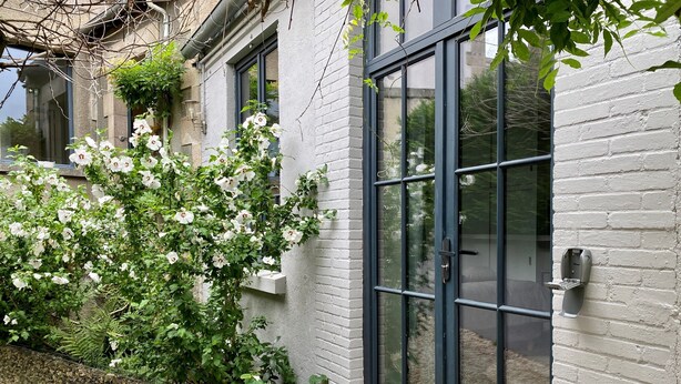 Un bâtiment à l’extérieur en briques blanches, doté d’une grande fenêtre à cadre noir et d’une porte avec une poignée.