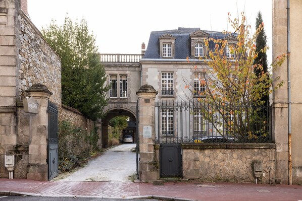 A stone building with a gated entrance, an archway, and a tree with autumn leaves. - La Villa Beaupeyrat (Limoges)