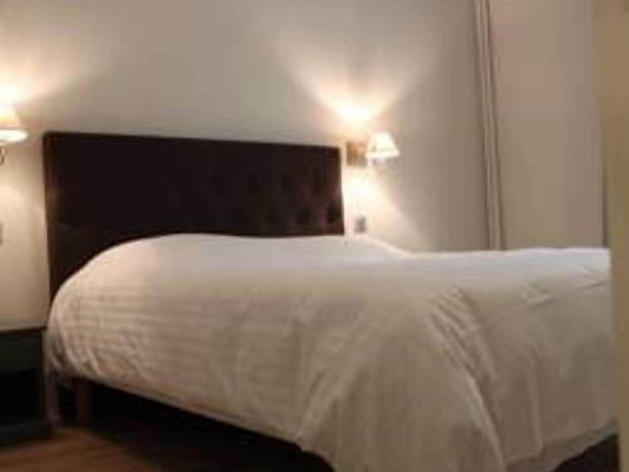 A neatly made bed in a hotel room with a dark headboard and two wall-mounted lamps.
