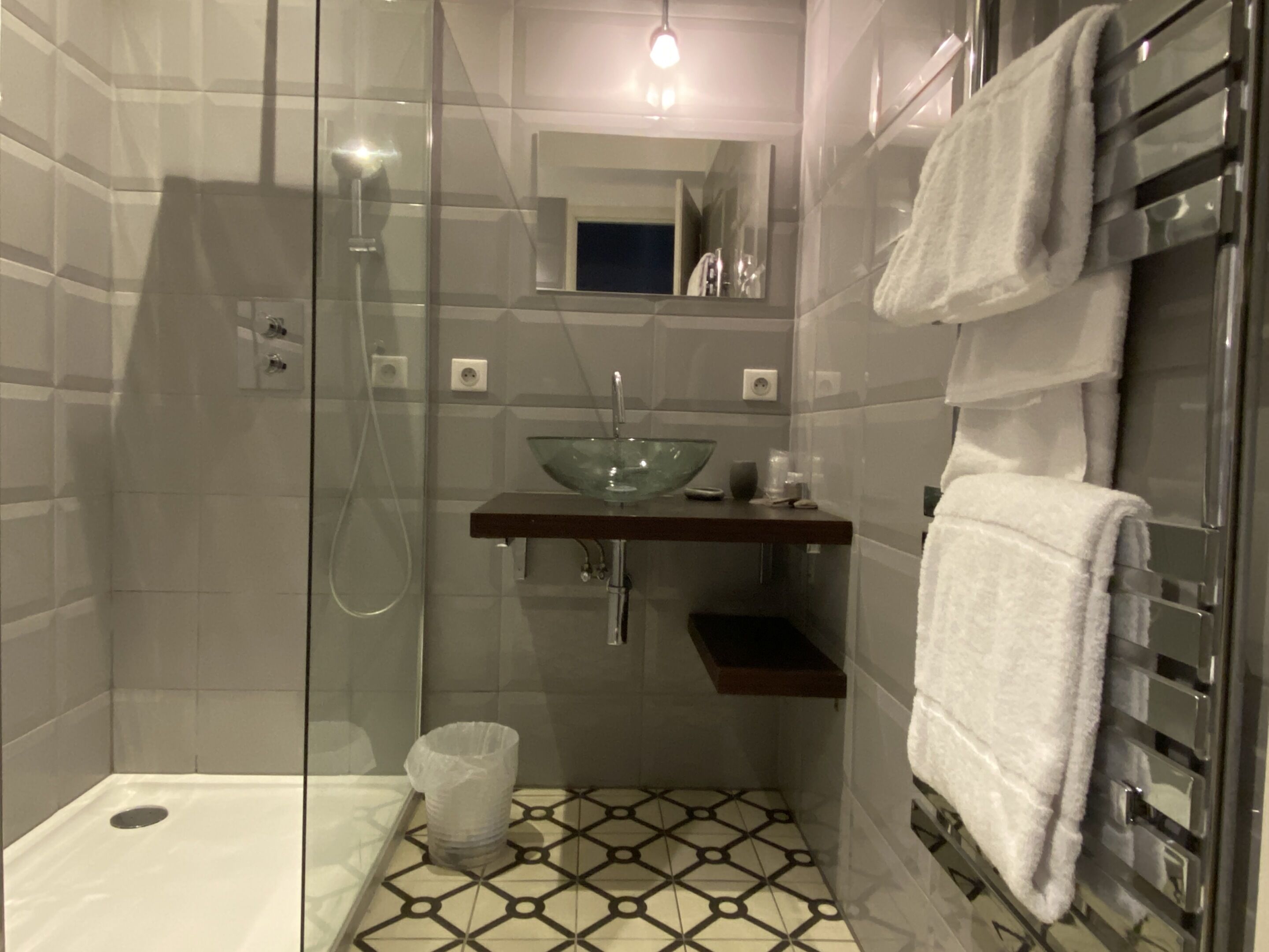 A modern bathroom with a glass-enclosed shower, a glass sink, and a towel rack.