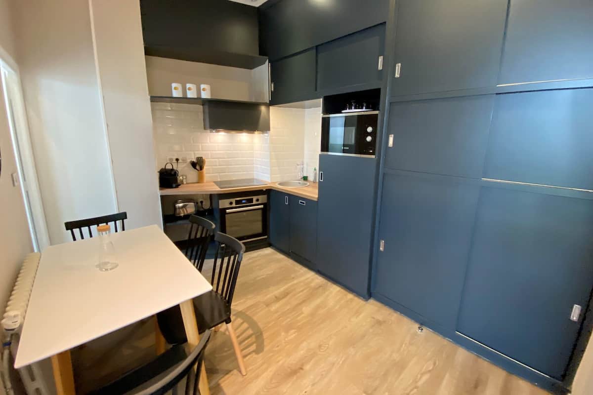 A compact kitchen with a dining area, featuring a white table, two chairs, a built-in oven, and a microwave.